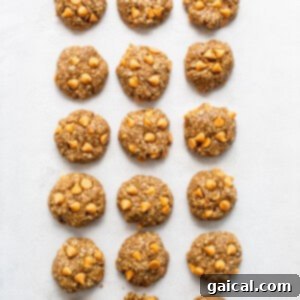 Raw cookie dough balls, slightly flattened, lined up on a baking sheet.