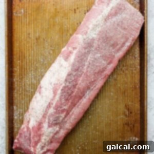 A raw rack of ribs seasoned with salt and pepper on a wooden cutting board.