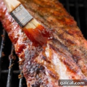 A spatula applying BBQ sauce to grilling ribs on a hot grill.