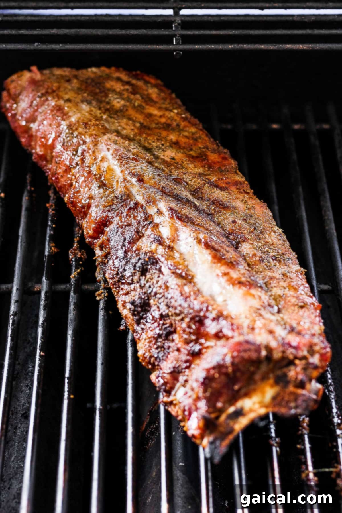 A rack of baby back ribs, seasoned and ready, cooking on the grill over indirect heat.