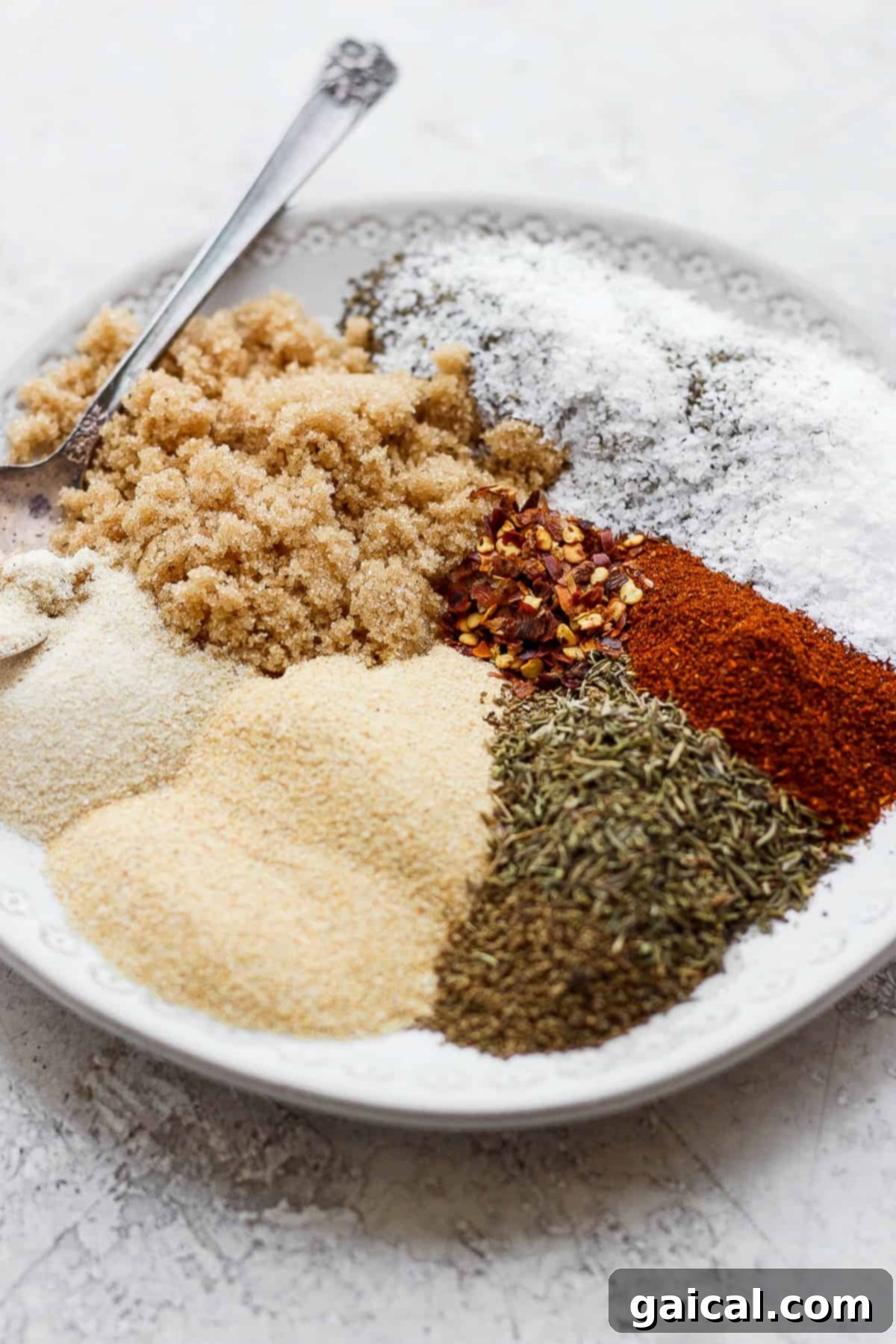 The Best Homemade Rib Rub Ingredients Assortment of dry rib rub ingredients meticulously arranged on a rustic wooden plate.