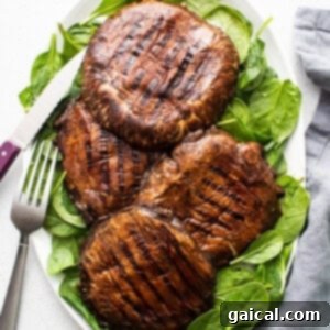Smoky Grilled Portobello Steaks 12 Grilled mushrooms on a plate with spinach and a fork, ready to be enjoyed.
