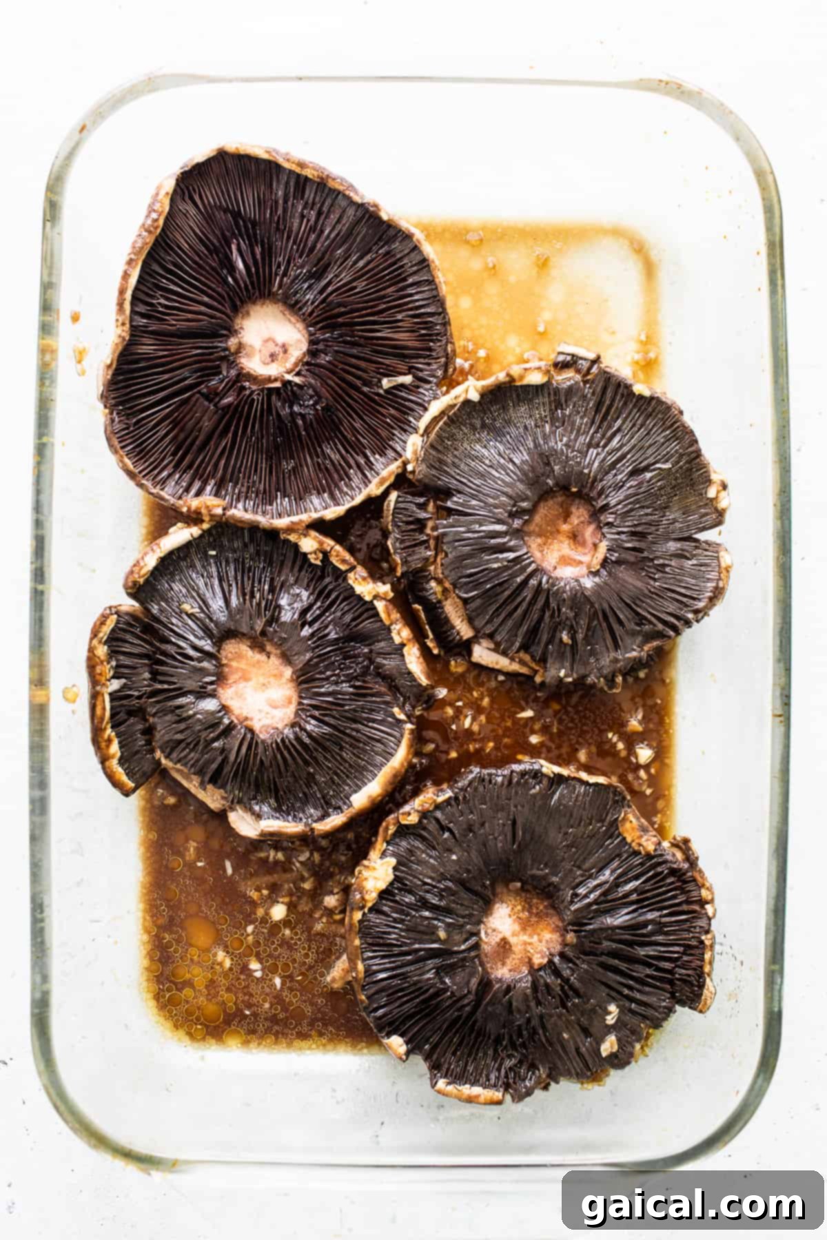 Smoky Grilled Portobello Steaks 4 Large portobello mushroom caps generously coated in a dark, glossy marinade in a shallow dish.