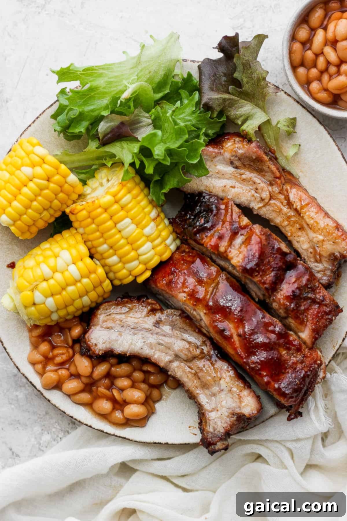 Fall-Off-The-Bone Baby Back Ribs (Grill or Oven) 2 A vibrant plate featuring perfectly cooked ribs, accompanied by corn on the cob, a fresh bean salad, and crisp lettuce greens, showcasing a complete and appetizing meal.