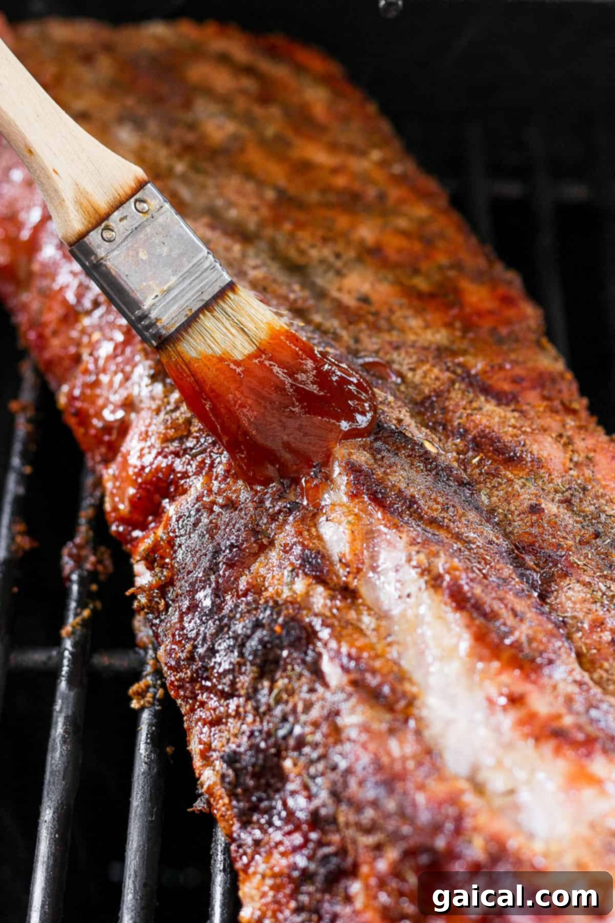 Fall-Off-The-Bone Baby Back Ribs (Grill or Oven) 6 A barbecue grill with a metal spatula resting on the grate, coated in rich, dark BBQ sauce, hinting at a delicious basting process.