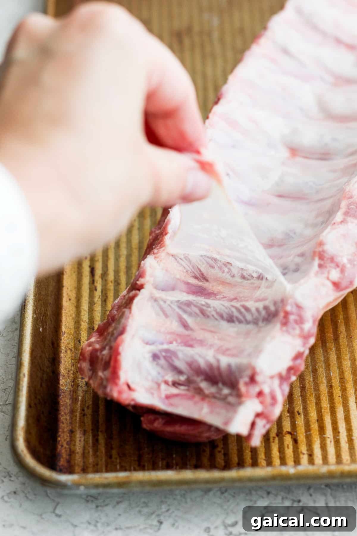 Fall-Off-The-Bone Baby Back Ribs (Grill or Oven) 3 A person carefully holds a rack of marinated baby back ribs on a tray, ready for cooking, highlighting the preparation stage of the recipe.