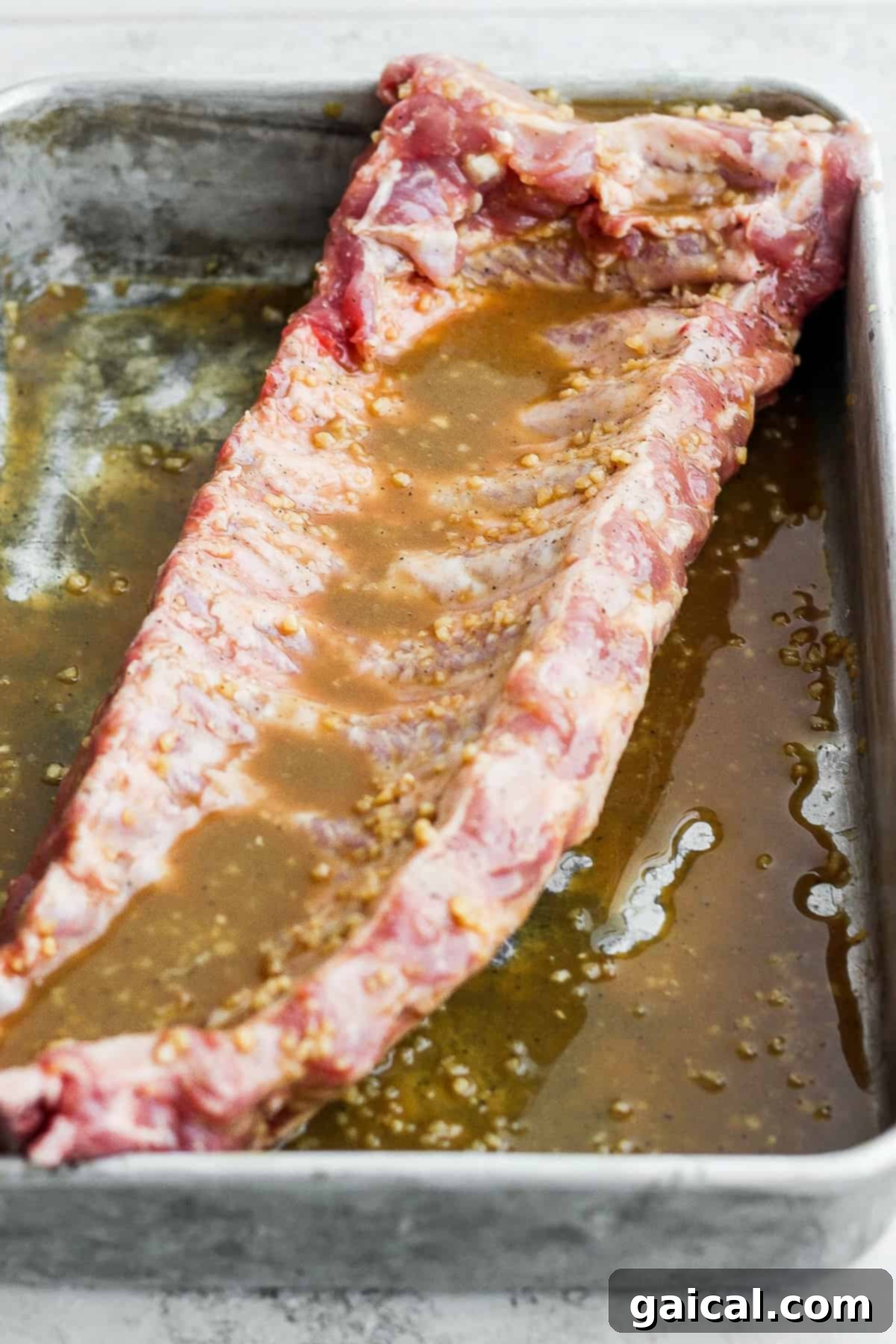 This classic rib marinade recipe is perfectly savory and sweet with only 5 ingredients -- an amazing complement to your baby back ribs. Enjoy! Rack of baby back ribs being marinated.