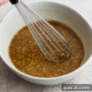 a hand holding a whisk in a bowl of brown liquid.