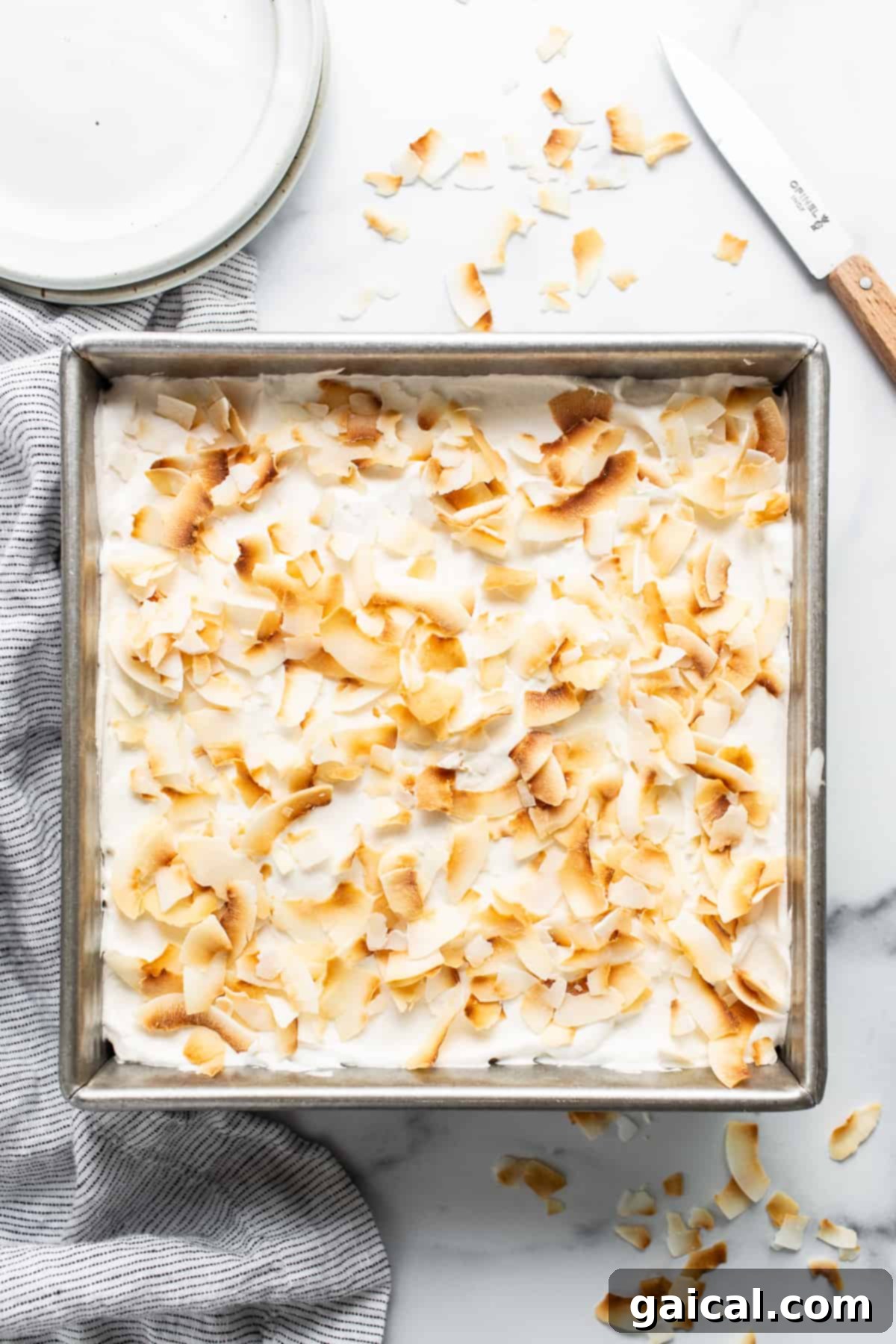Creamy Coconut Dream Bars 6 A pan filled with beautifully assembled coconut cream pie bars, generously topped with whipped cream and toasted coconut flakes.