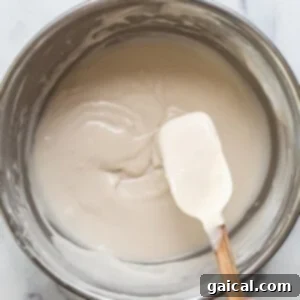 a hand holding a wooden spoon over a bowl of cream.