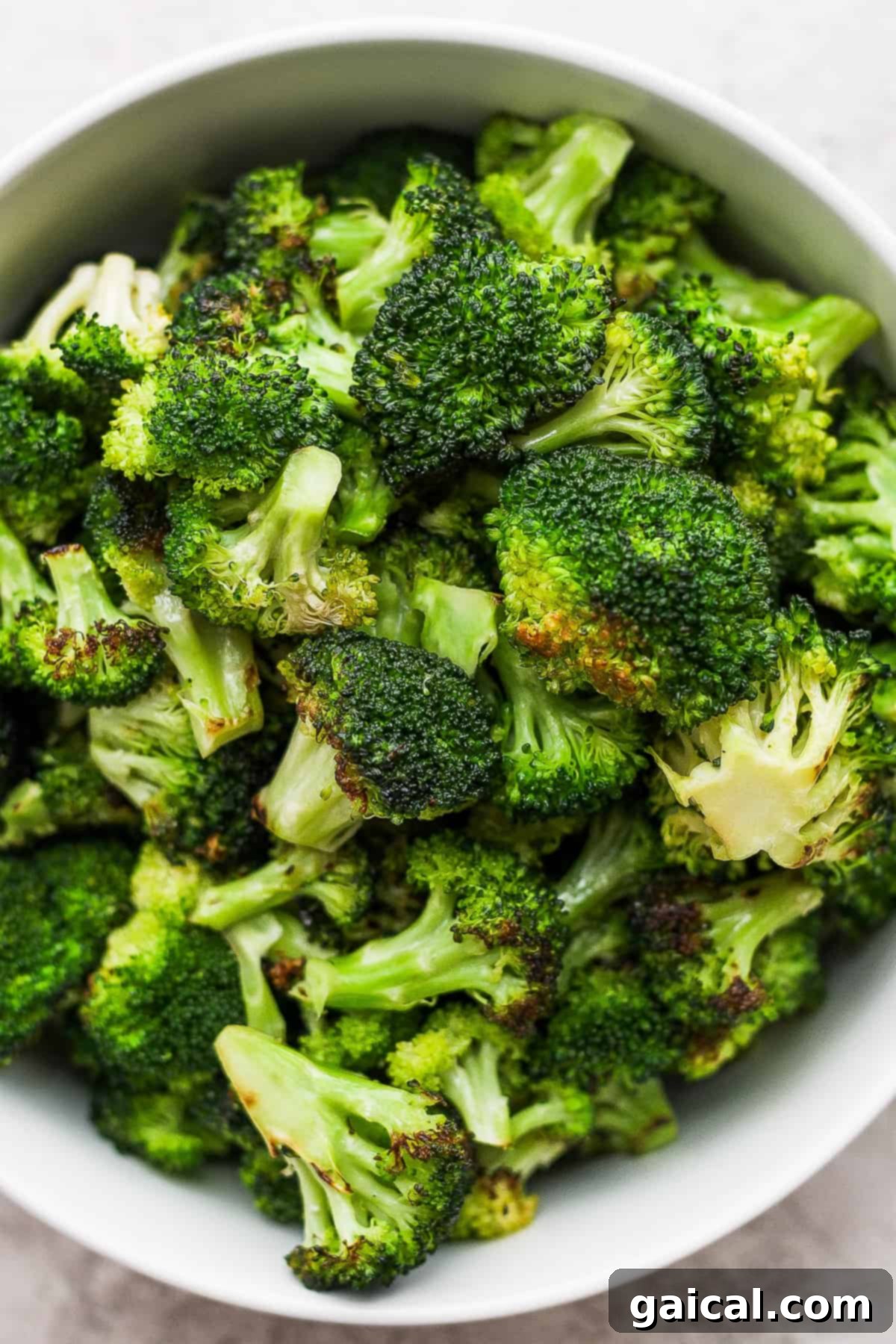 Charred Broccoli Perfection 2 A white bowl filled with perfectly charred and tender grilled broccoli florets, resting on a rustic wooden table, invitingly ready to be served.