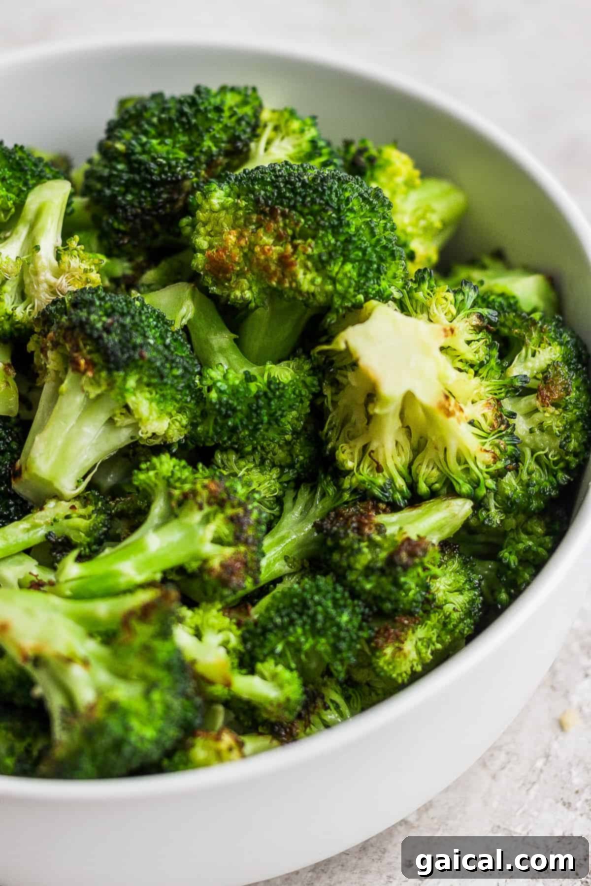 Charred Broccoli Perfection 7 A crisp white bowl overflowing with vibrant green grilled broccoli florets, perfectly charred and tender, sits invitingly on a clean white surface, ready to be enjoyed as a healthy and flavorful side dish.