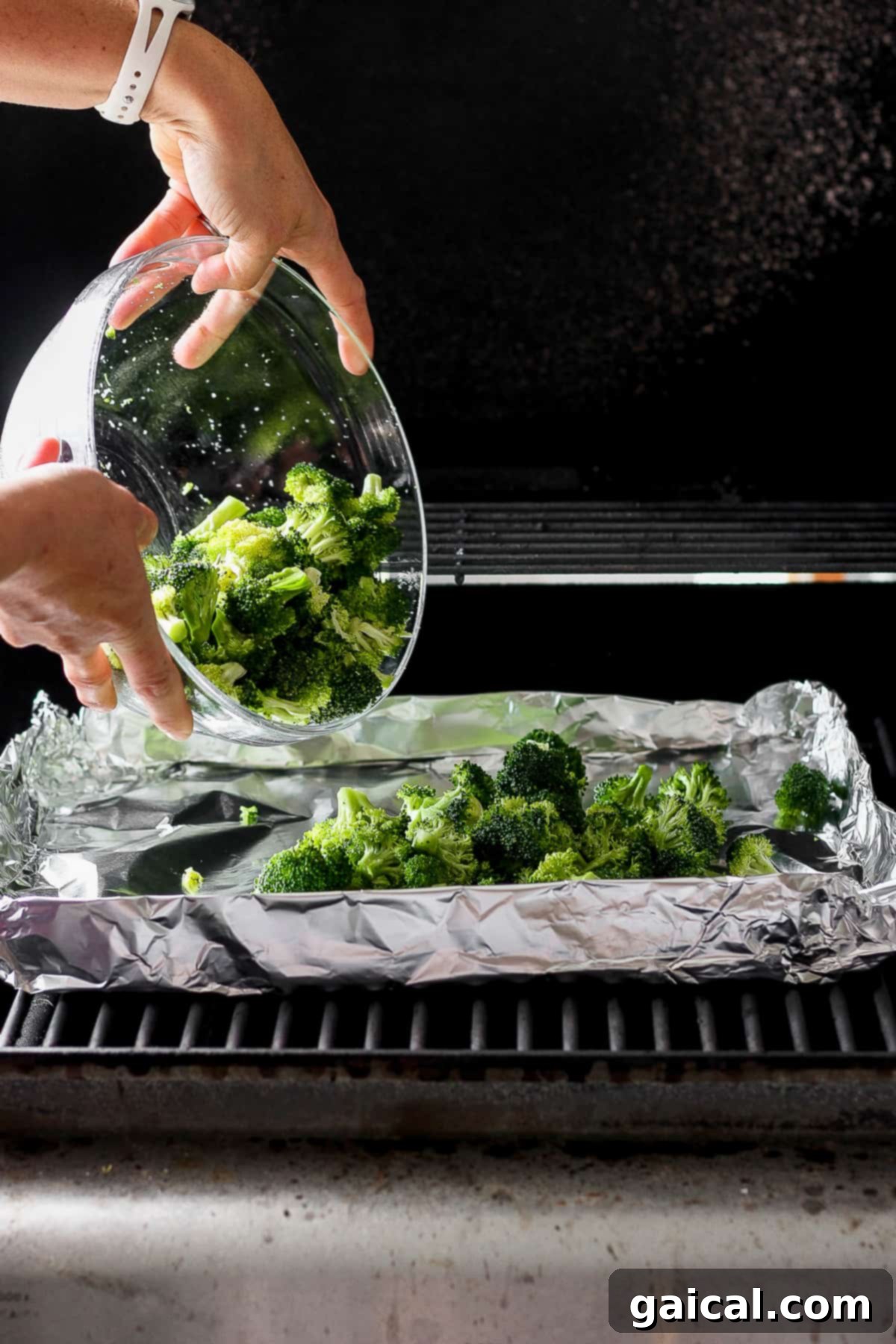 Charred Broccoli Perfection 4 A skilled hand carefully places vibrant green broccoli florets onto a grill, set on a piece of tin foil, ready to be transformed into a delicious charred side dish.