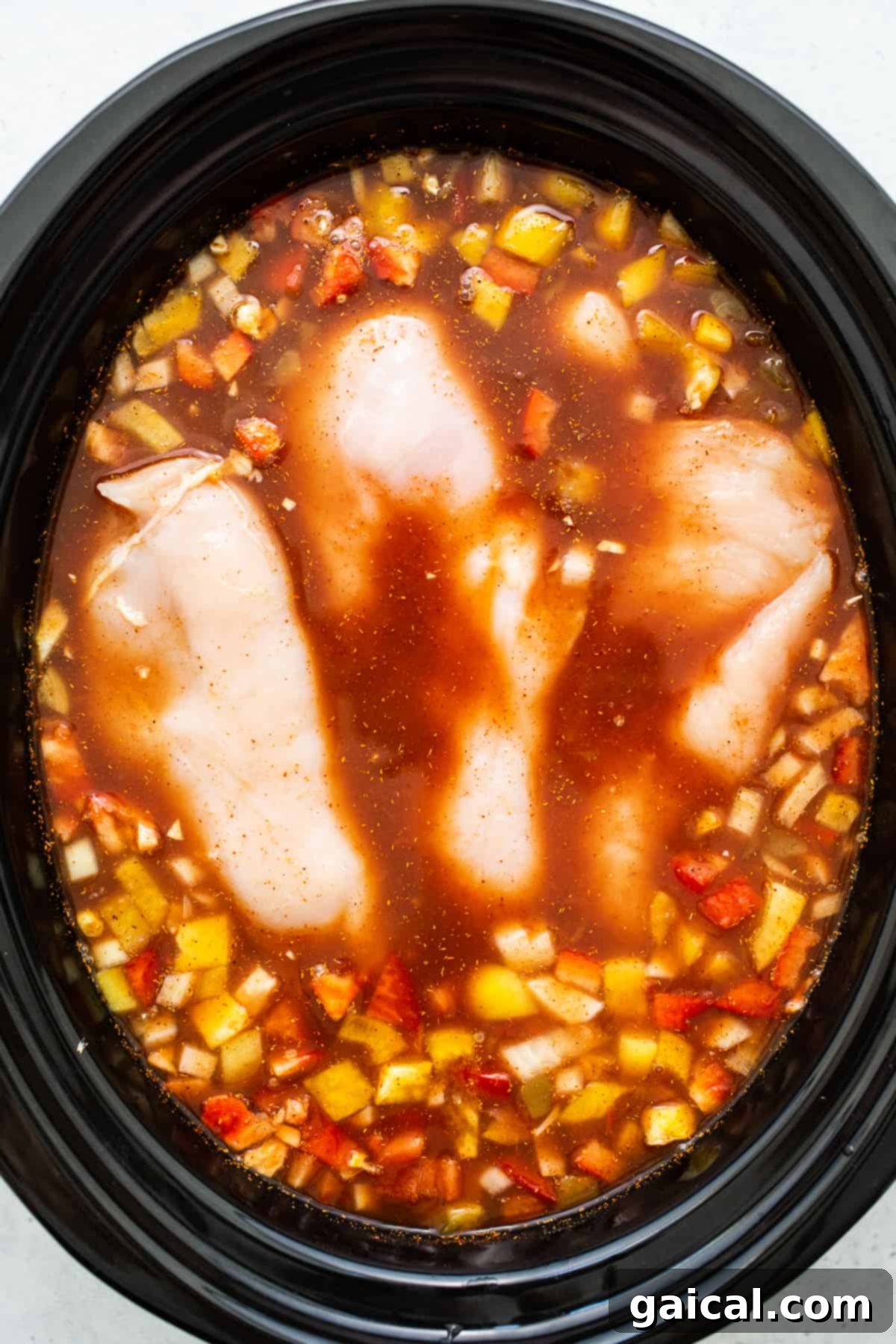 Chicken Breasts Cooking in Tortilla Soup Tender chicken breasts submerged in a rich, simmering tomato broth within a slow cooker.