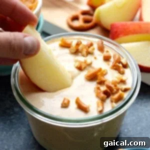 A person is dipping a pretzel into a bowl of pumpkin yogurt dip, highlighting its appetizing texture.