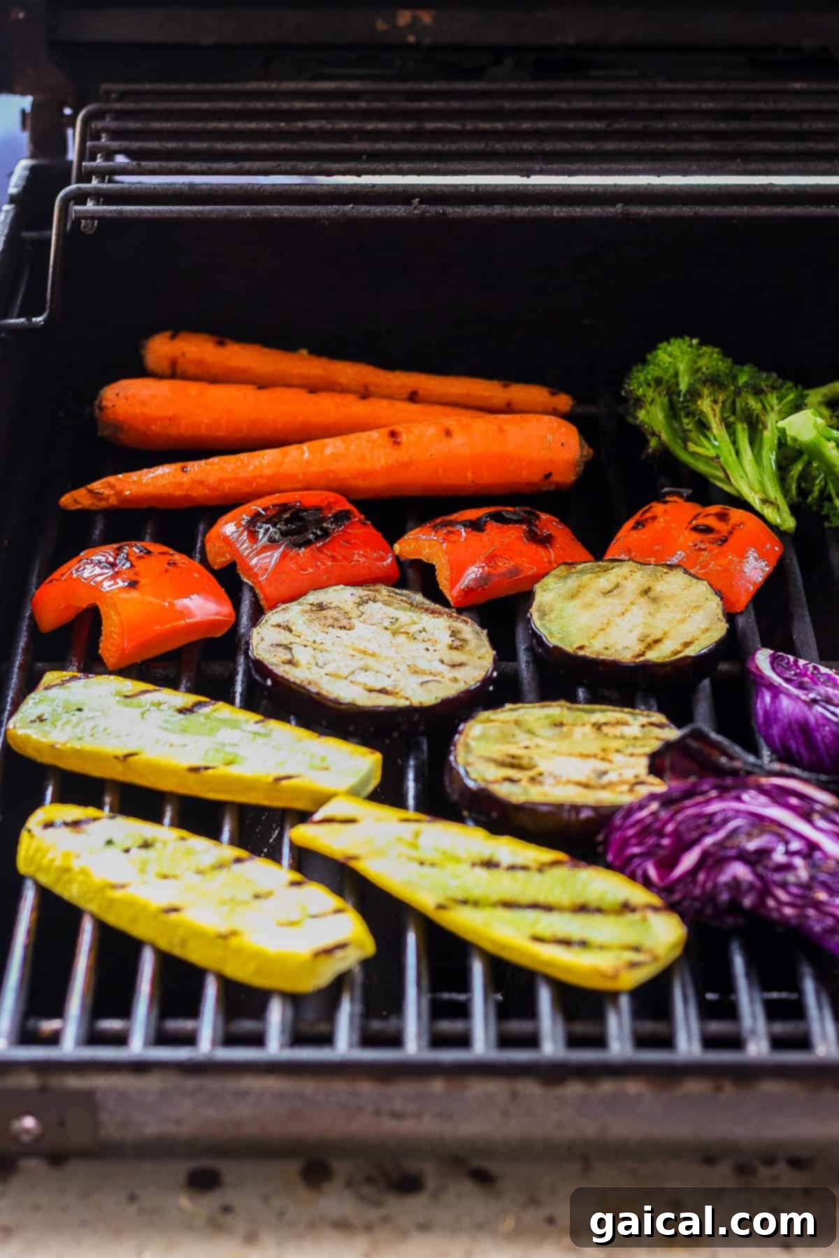 A close-up shot of various colorful vegetables including carrots, broccoli, and peppers cooking on a hot outdoor grill, showing perfect charring.
