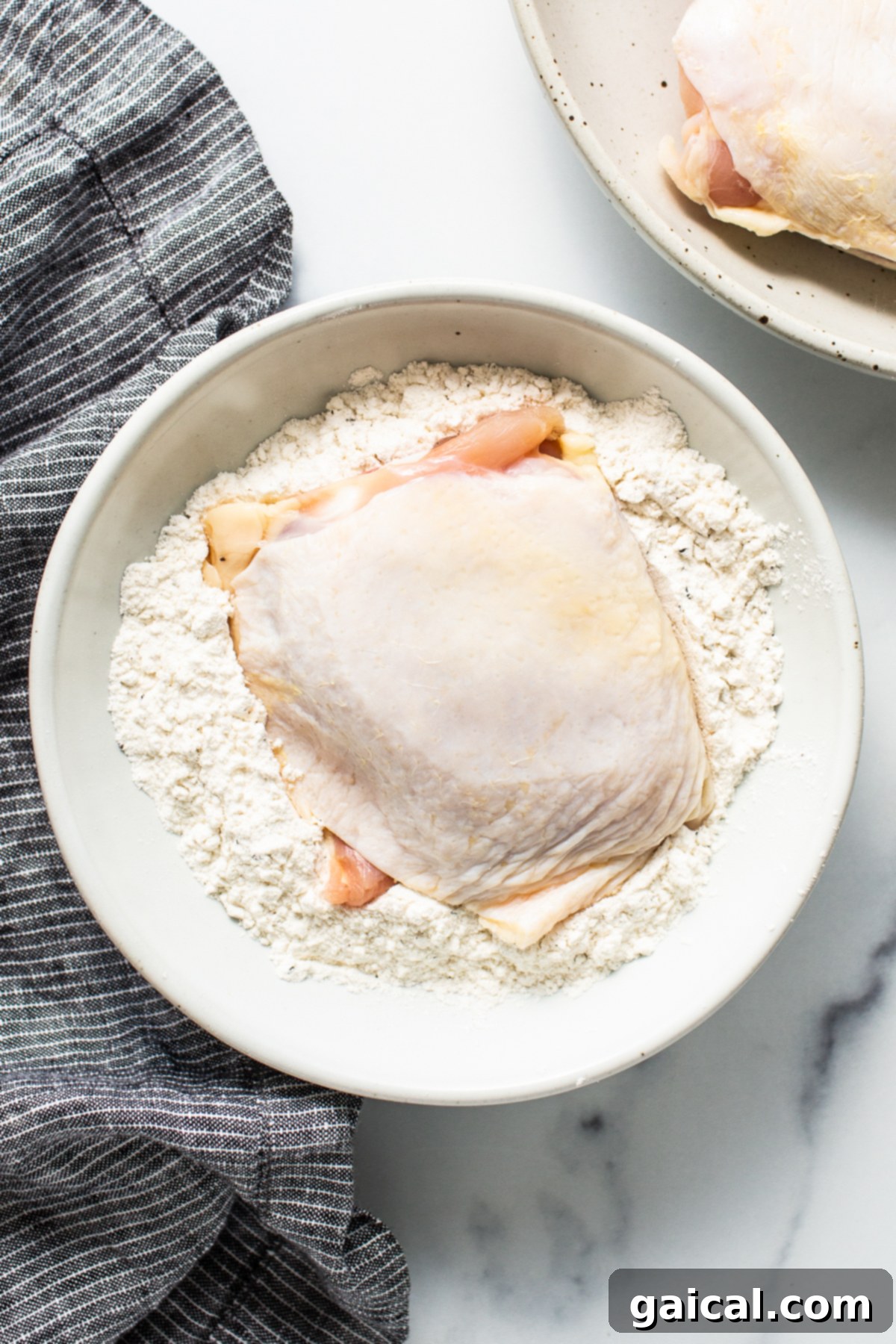 Dynamite Chicken Thighs 3 raw chicken thigh being dredged in flour.