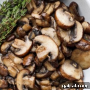 roasted mushrooms in a white bowl with a sprig of thyme.
