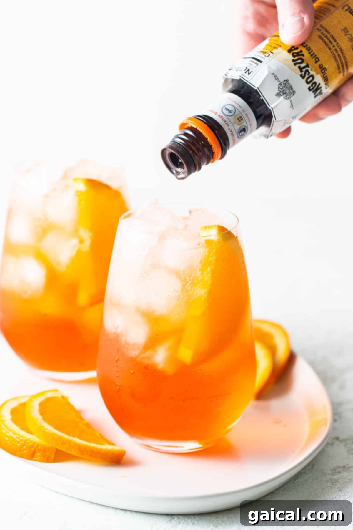 Adding orange bitters for an extra layer of complexity. A dash of orange bitters being added to an Aperol Spritz, enhancing its flavor profile.