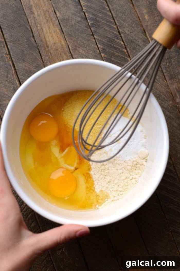 Close-up of cornmeal whole wheat pancake batter being stirred in a large ceramic bowl, ready for cooking.