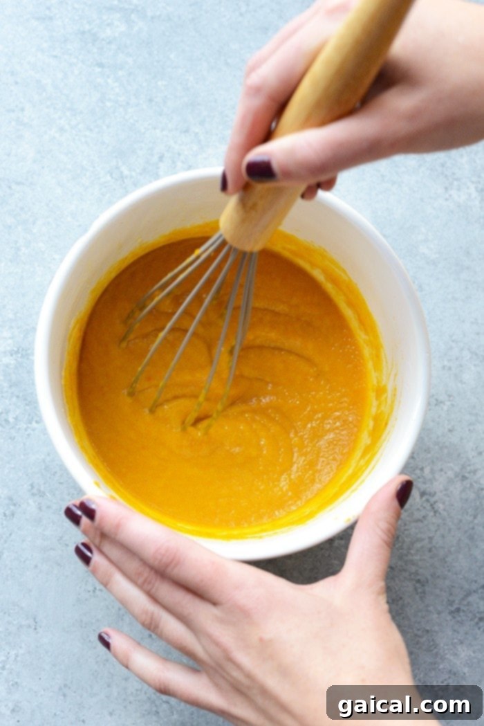 Guilt-Free Chocolate Pumpkin Muffins 3 Smooth, vibrant pumpkin puree being vigorously whisked in a glass bowl, illustrating a crucial step in preparing the wet ingredients for pumpkin muffins.