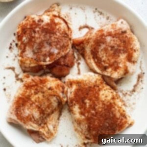 Four chicken breasts on a white plate with spices.