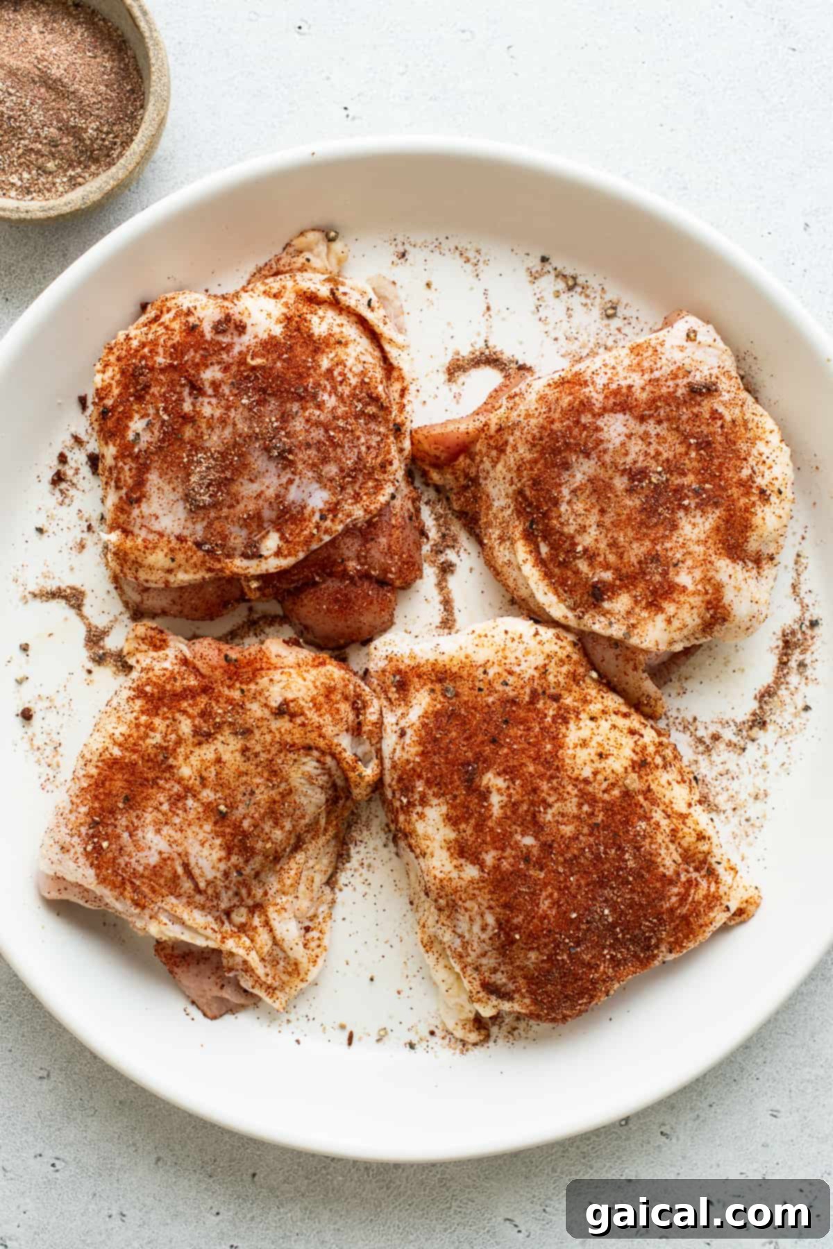 Seasoned chicken thighs on a plate, ready for cooking