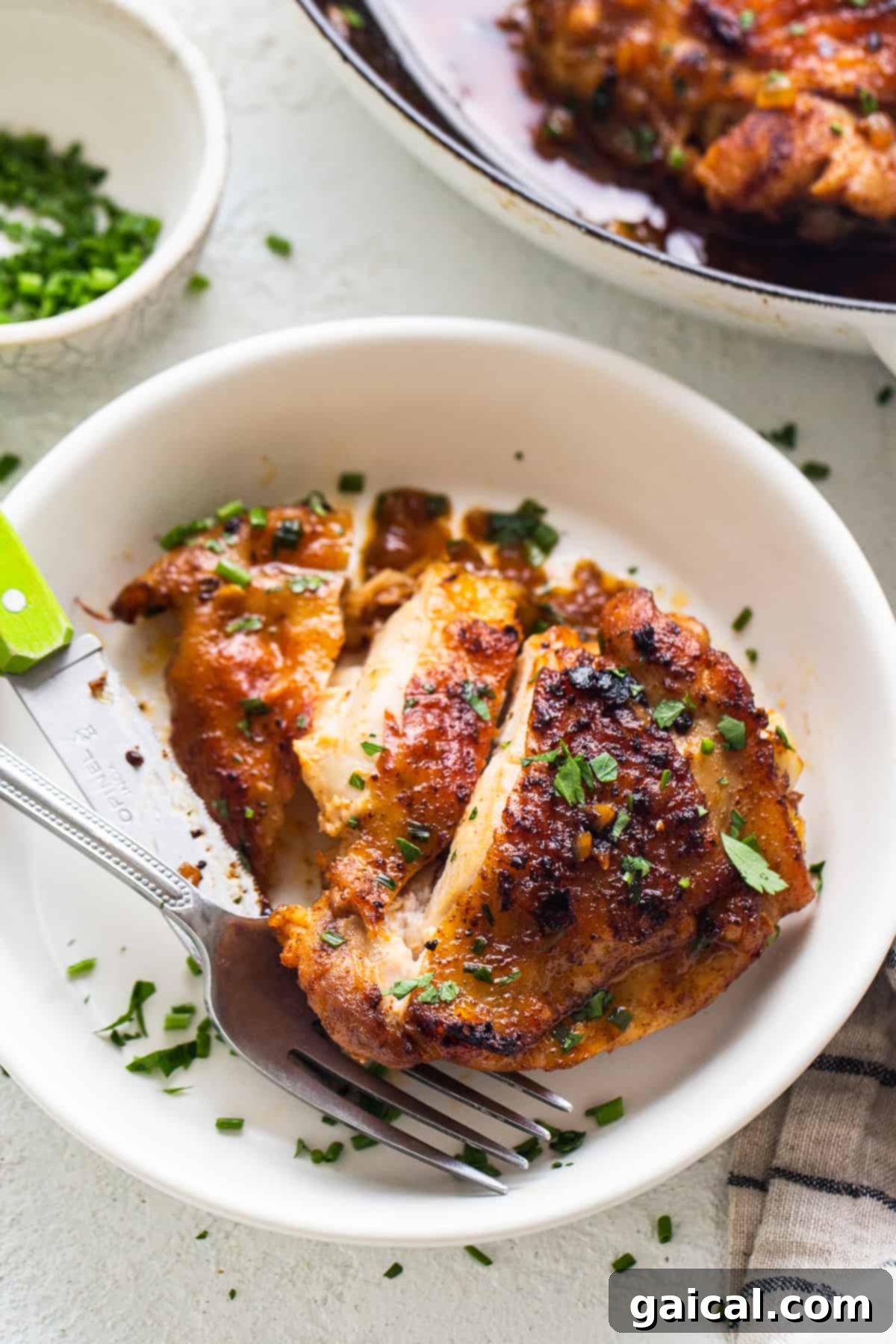 Cooked cast iron chicken thigh on a white plate with fork