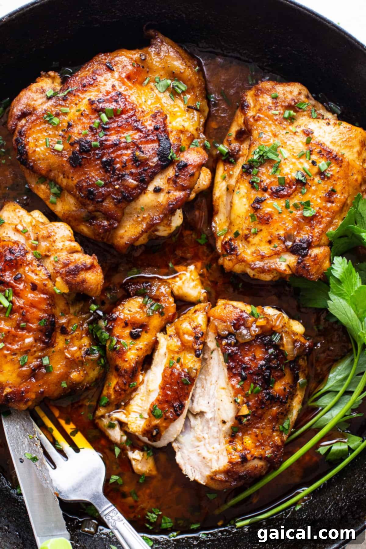 Seven cooked cast iron chicken thighs stacked in a pan with sauce