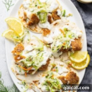 Fish tacos on a white plate with lemon wedges.