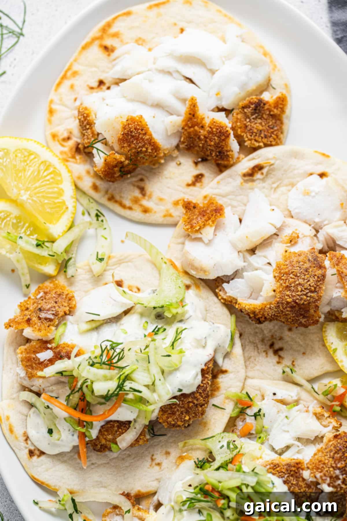 Crispy Air Fryer Fish Tacos 5 Three fish tacos on a plate with lemon wedges.