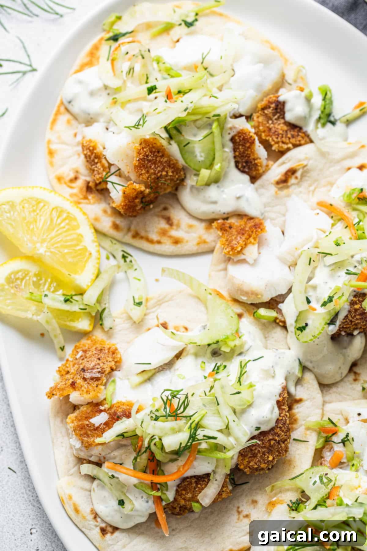 Crispy Air Fryer Fish Tacos 6 Fish tacos with slaw and lemon wedges on a white plate.