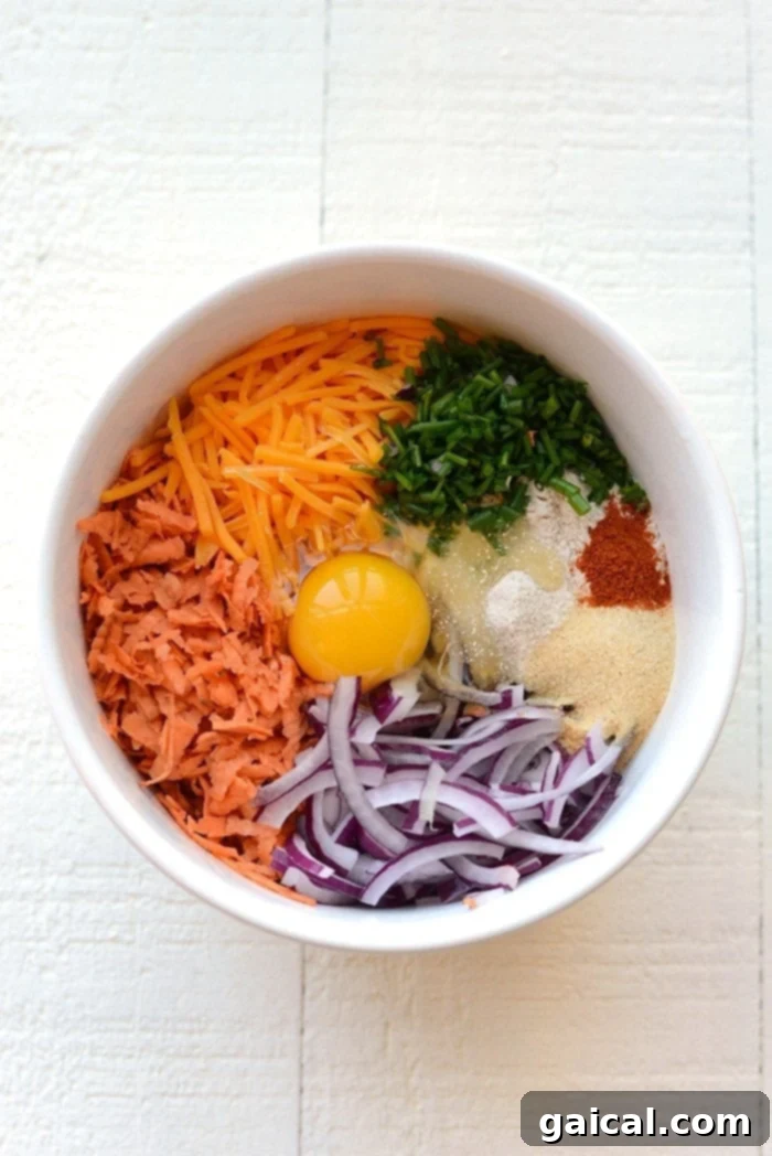Fresh Ingredients for Sweet Potato Hash Browns A large mixing bowl filled with freshly grated sweet potatoes, shredded cheddar cheese, sliced red onion, and chopped chives, ready to be combined for hash browns.