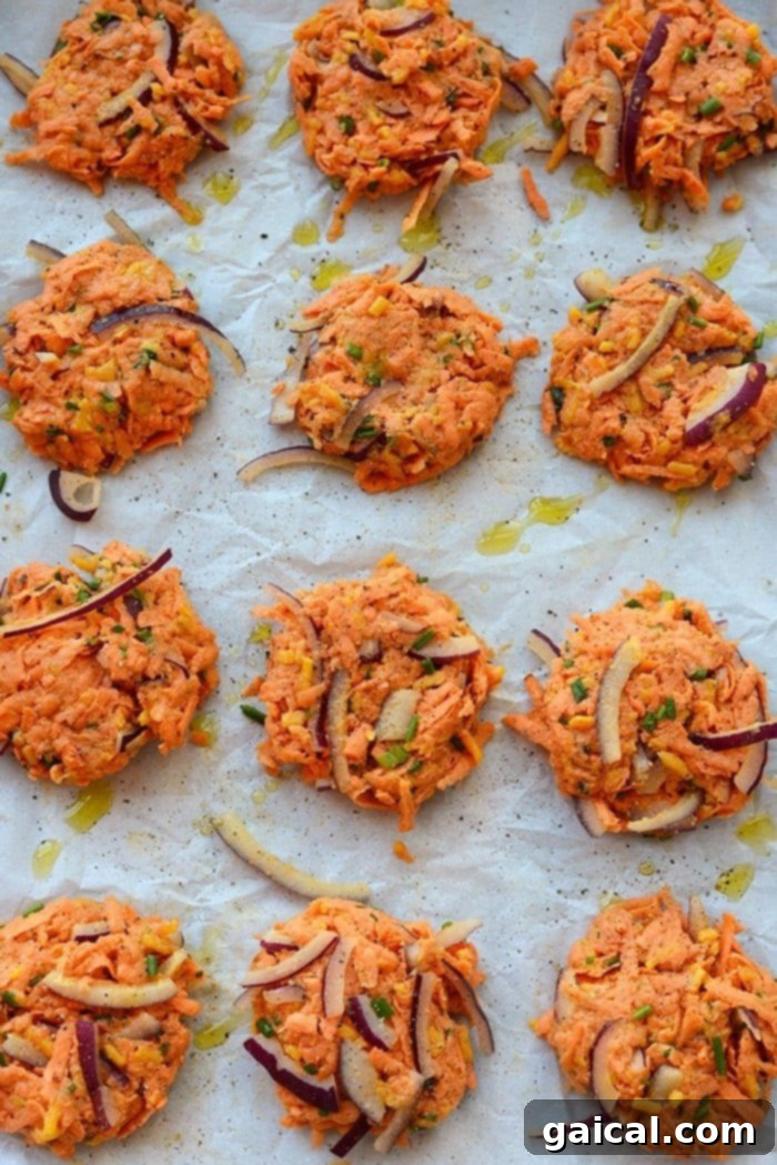 Sweet Potato Hash Browns Ready for Baking Unbaked sweet potato hash brown fritters perfectly shaped on a parchment-lined baking sheet, drizzled with olive oil and ready for the oven.