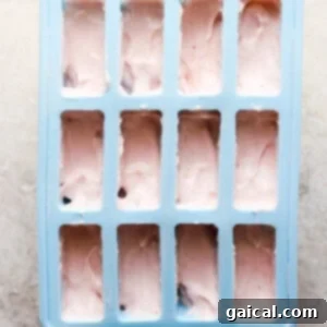 Protein-Packed Strawberry Shortcake Ice Cream Bars 11 A blue ice cube tray filled with pink, creamy ice cream mixture, ready for freezing.