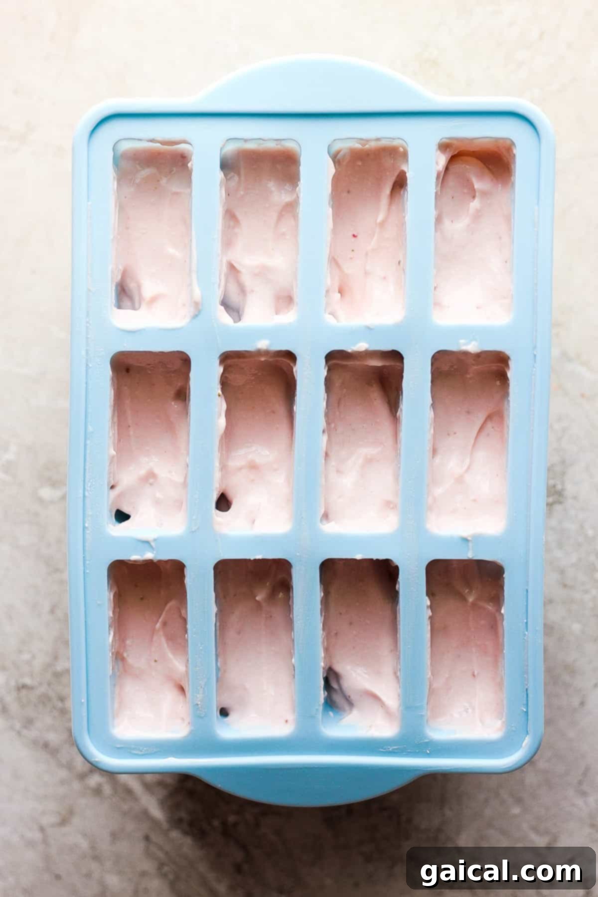 Protein-Packed Strawberry Shortcake Ice Cream Bars 6 A blue ice cube tray filled with pink, creamy ice cream mixture, ready for freezing.