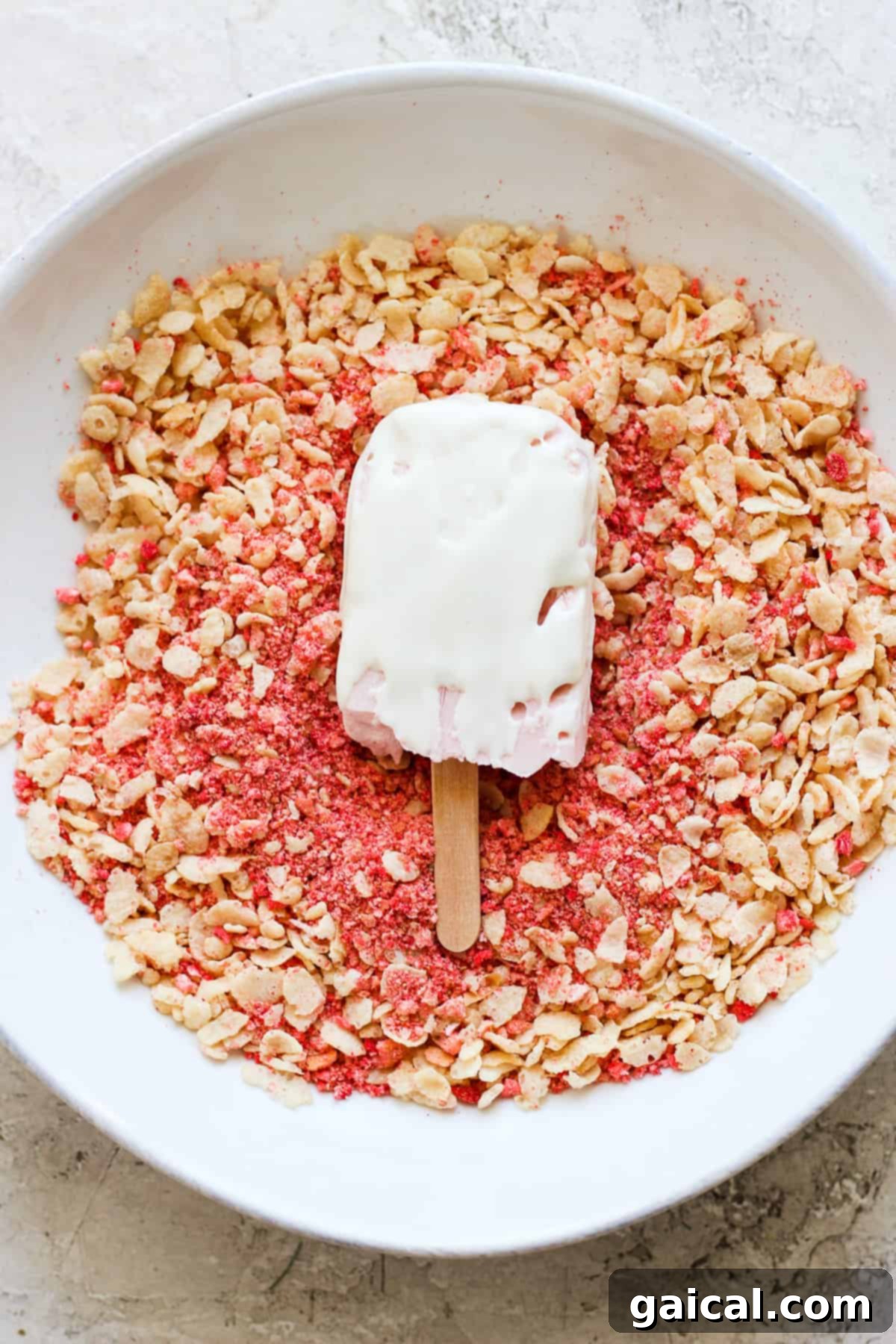 Protein-Packed Strawberry Shortcake Ice Cream Bars 7 A bowl of pink granola with a strawberry popsicle resting on top, garnished with fresh berries.