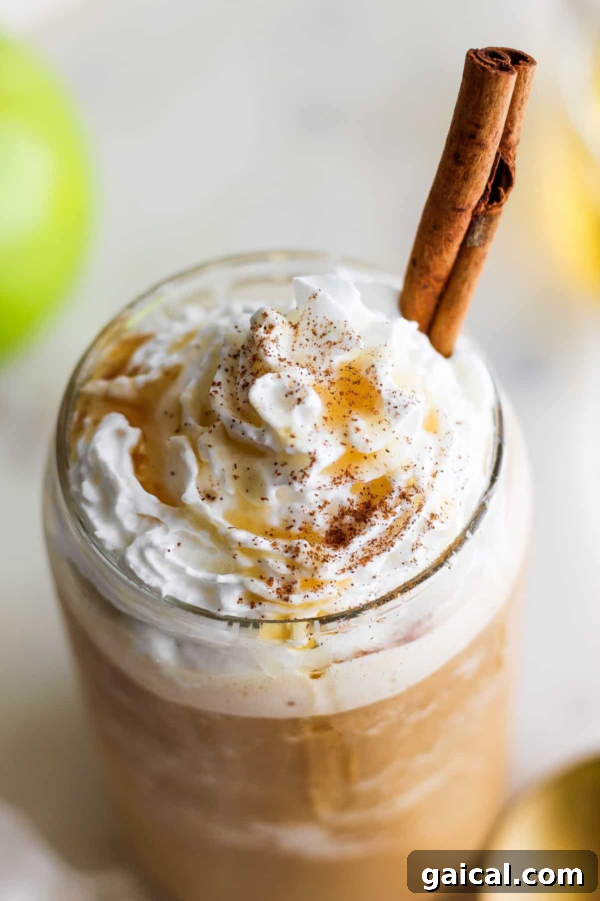 Maple Kissed Apple Crisp Oatmilk Blend 8 An apple latte with whipped cream and a cinnamon stick, presented beautifully.