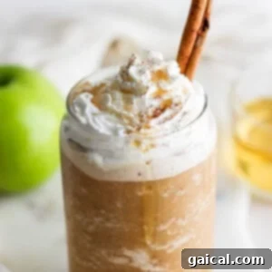 A mug filled with apple crisp oatmilk frappuccino, topped with whipped cream and a cinnamon stick.