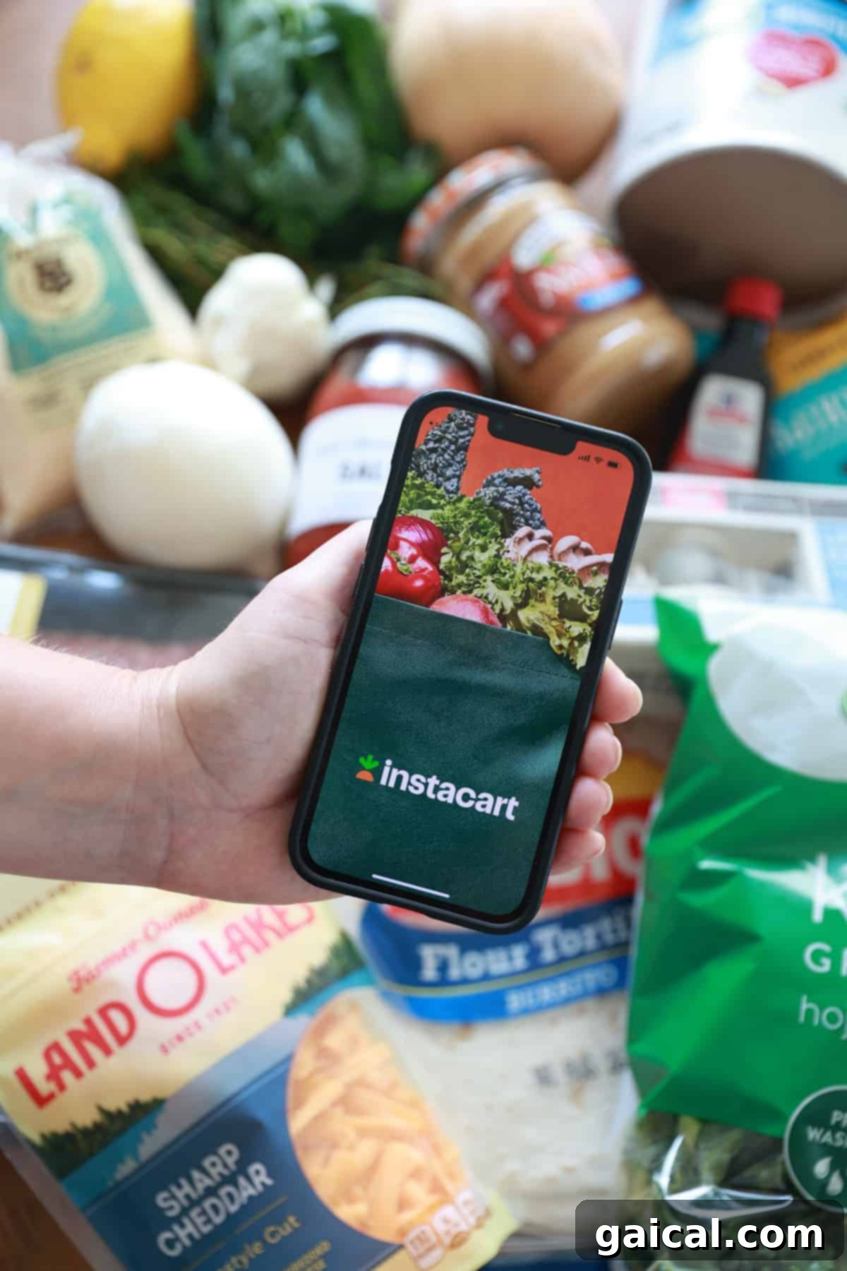 A person holding a smartphone next to bags of fresh groceries delivered by Instacart.