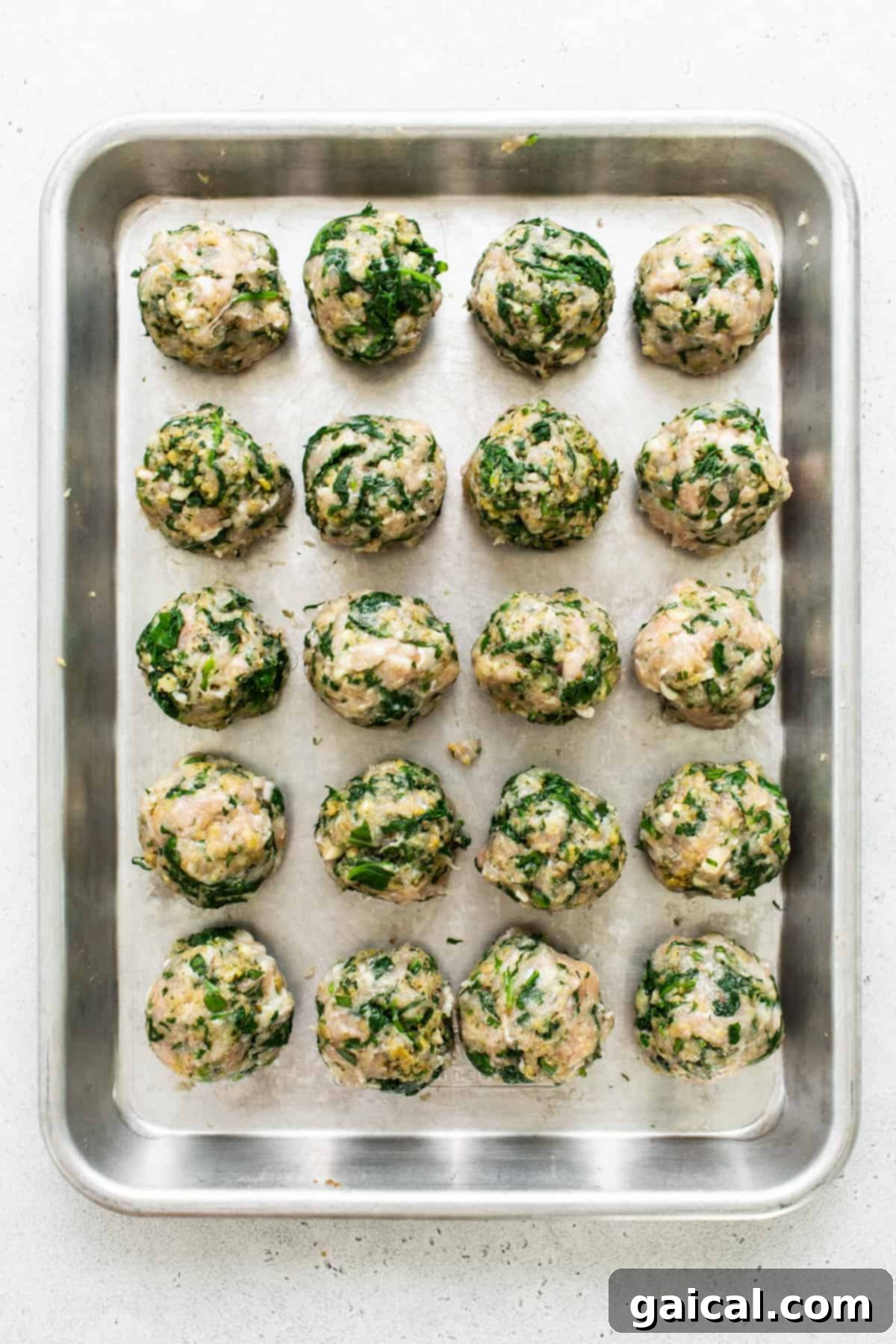 Raw spinach and mushroom meatballs on a baking sheet, ready for cooking.