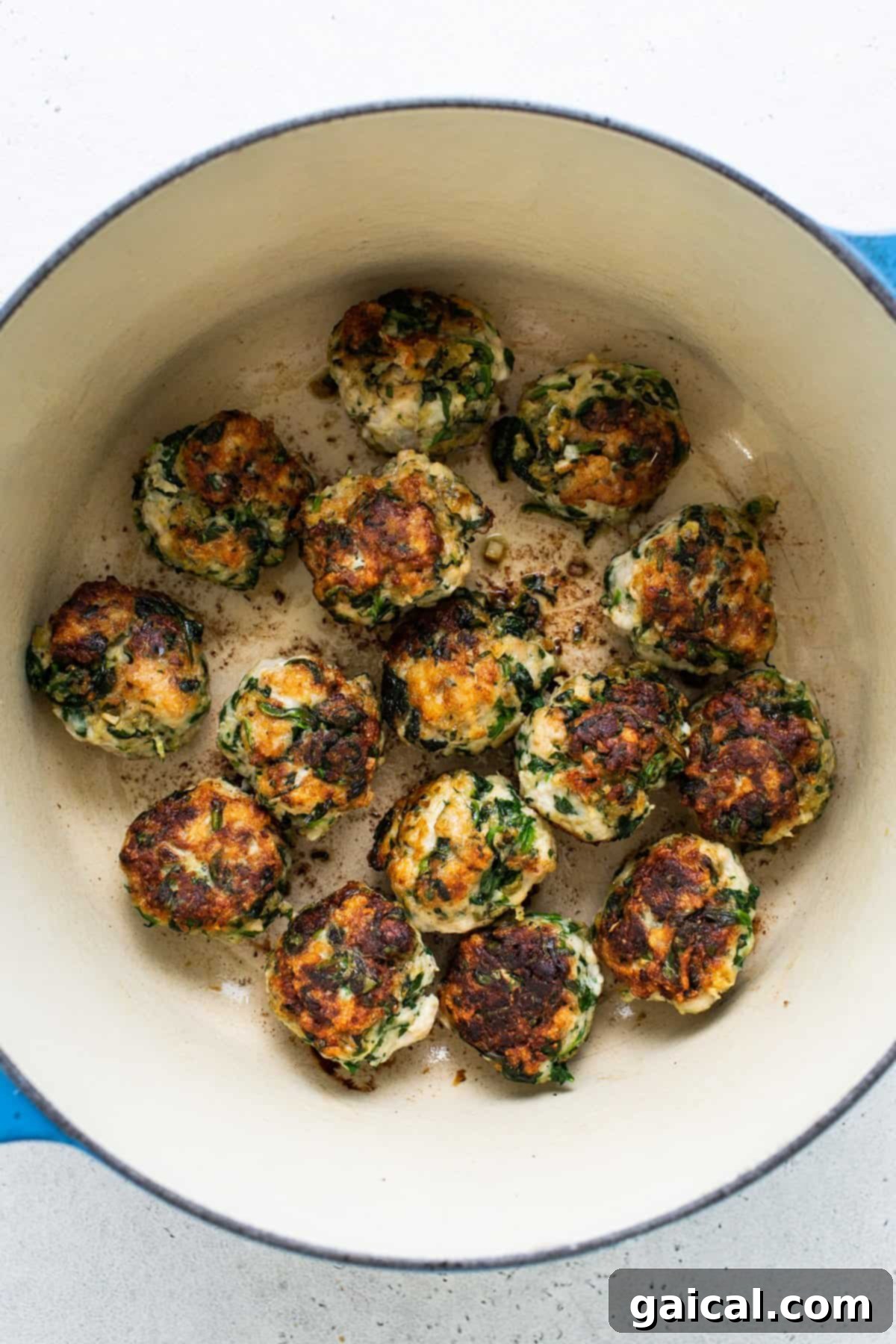 Seared chicken and spinach meatballs cooking in a blue pot.