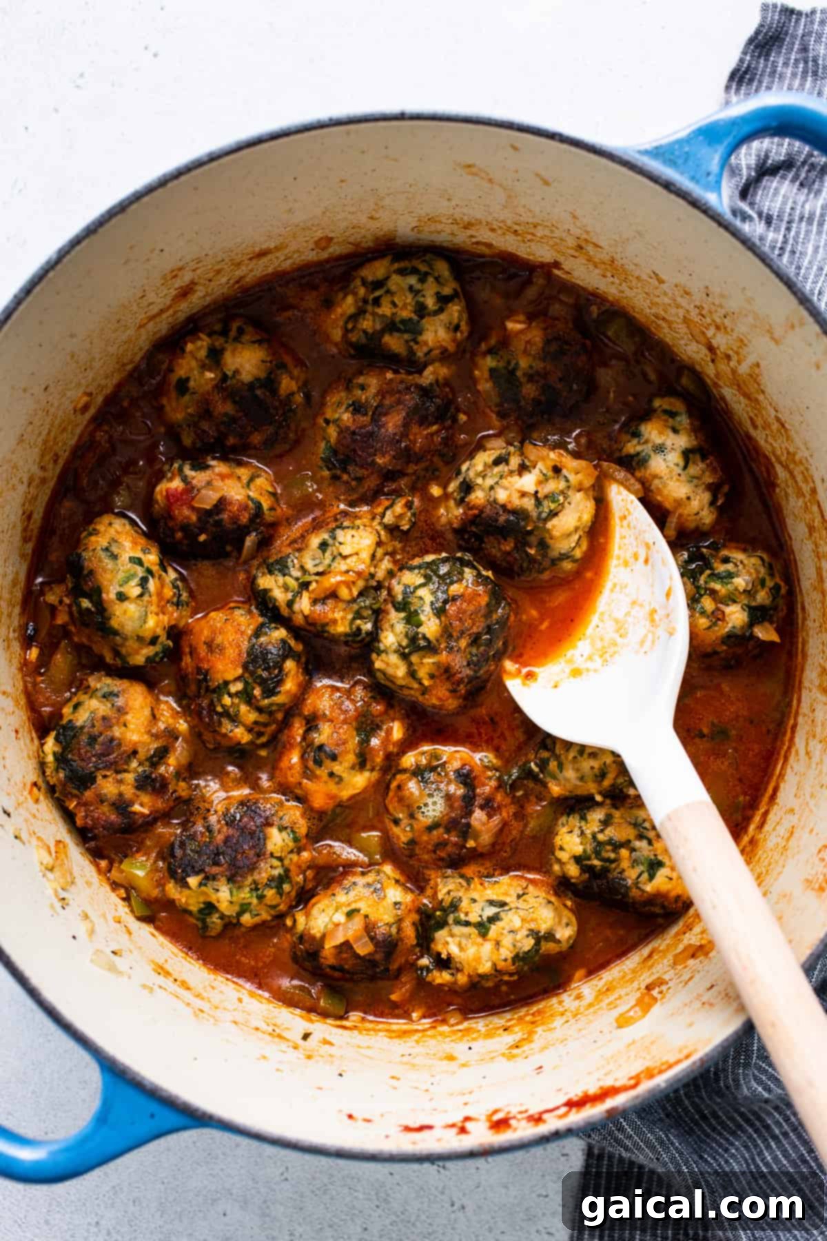 Tender chicken meatballs simmering in a rich tomato sauce with a spoon for serving.