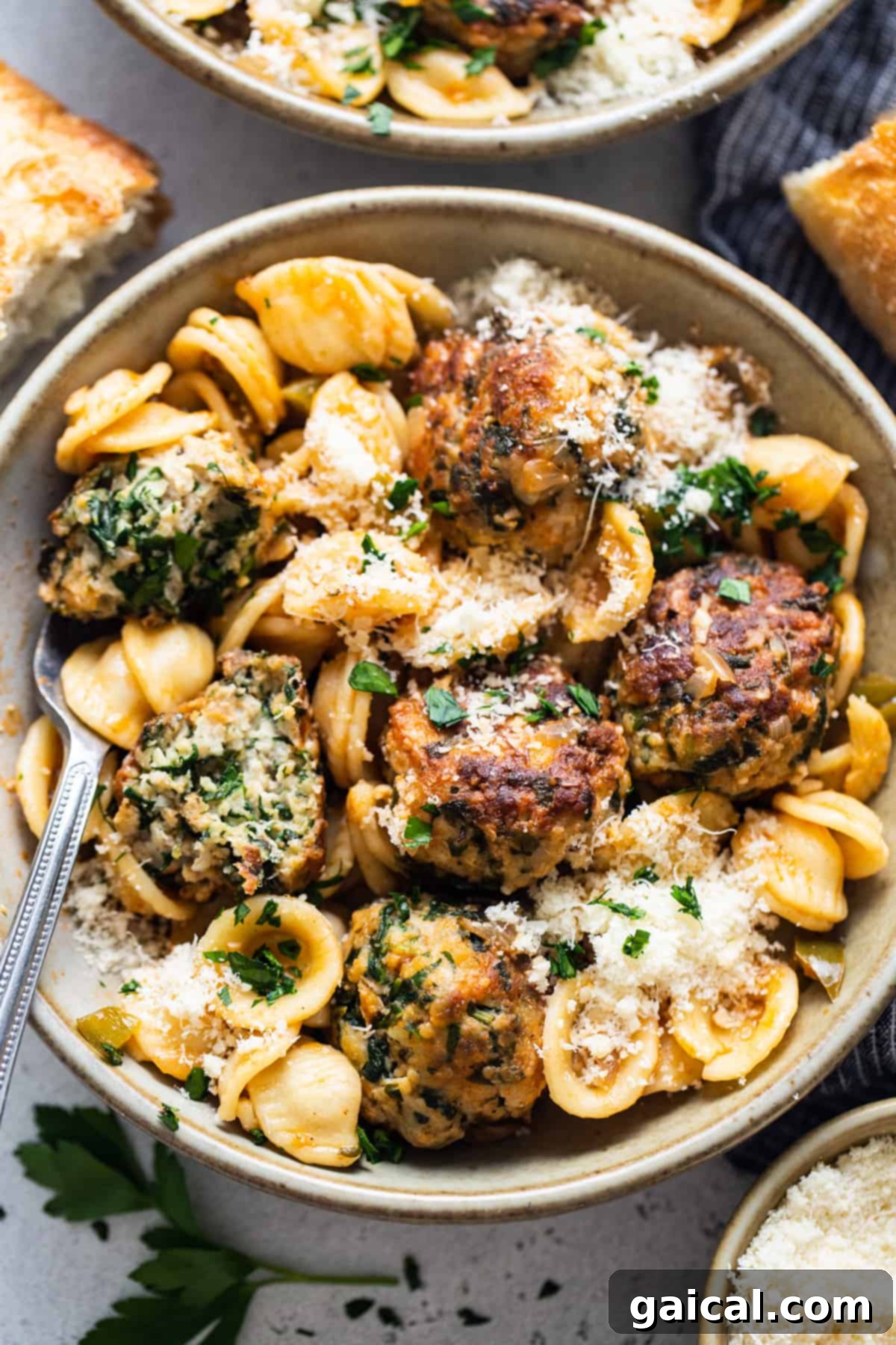 A close-up of a bowl of pasta with Tuscan chicken meatballs, garnished with Parmesan cheese.