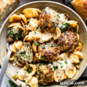 A bowl of pasta with meatballs and spinach.