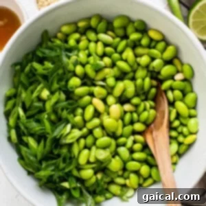 Golden Honey Chili Air Fryer Salmon Bites 11 Preparation of the edamame salad, showing the mixture of green onions, sesame oil, rice vinegar, salt, sesame seeds, and lime juice being tossed with the edamame.