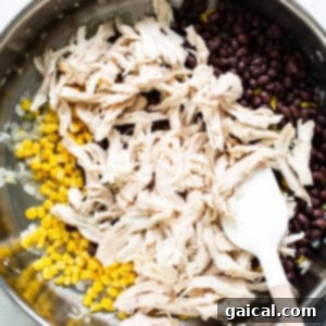 Shredded chicken, black beans, and frozen corn being mixed in a skillet with a wooden spoon.