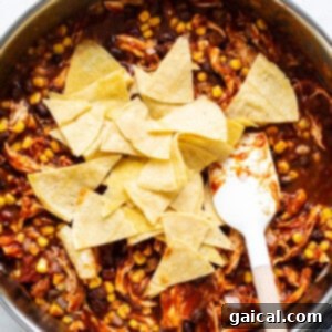 Mexican chicken enchilada mixture in a pan with tortilla triangles being folded into the sauce.