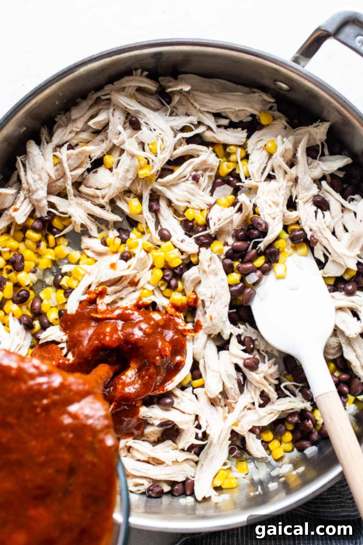 Chicken, black beans, and corn simmering in a rich red sauce within a large skillet, ready for the oven.