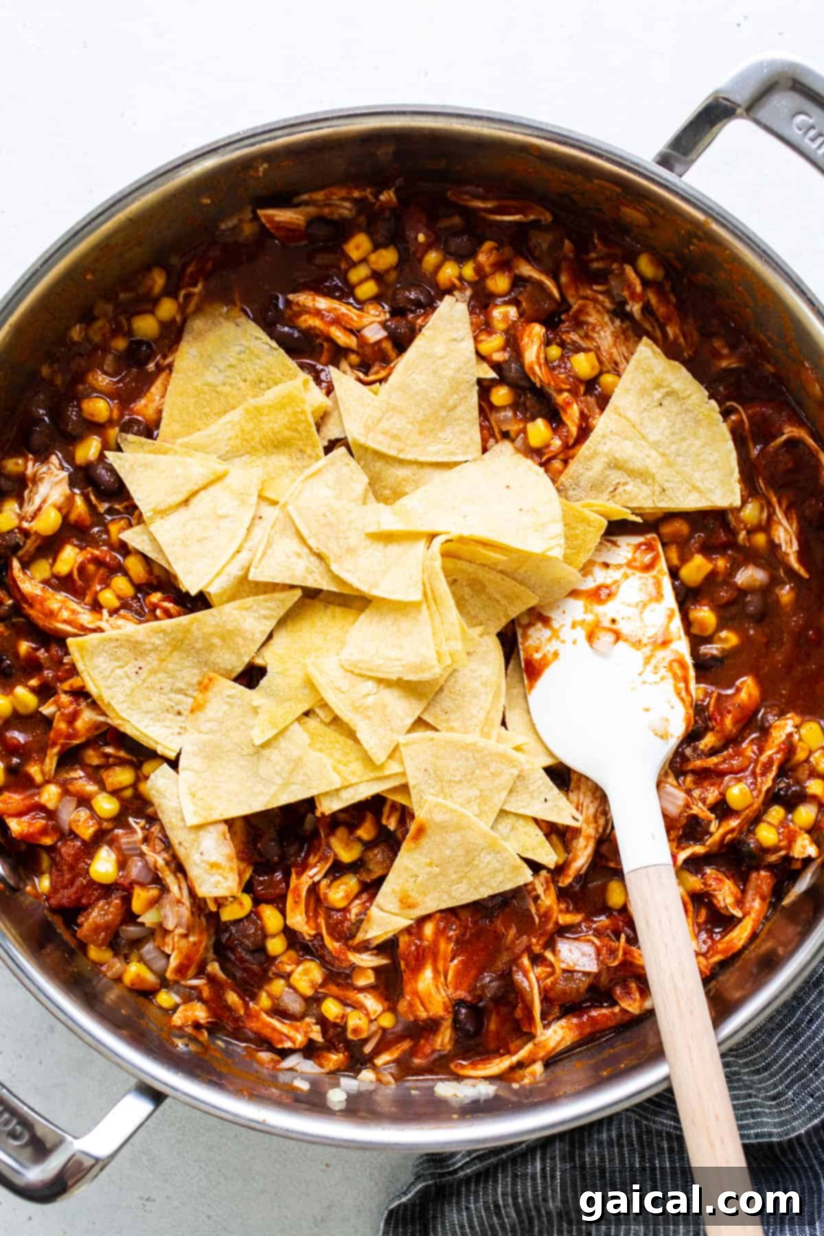 Mexican chicken enchilada skillet filled with ingredients and topped with cheese and tortilla pieces before baking.